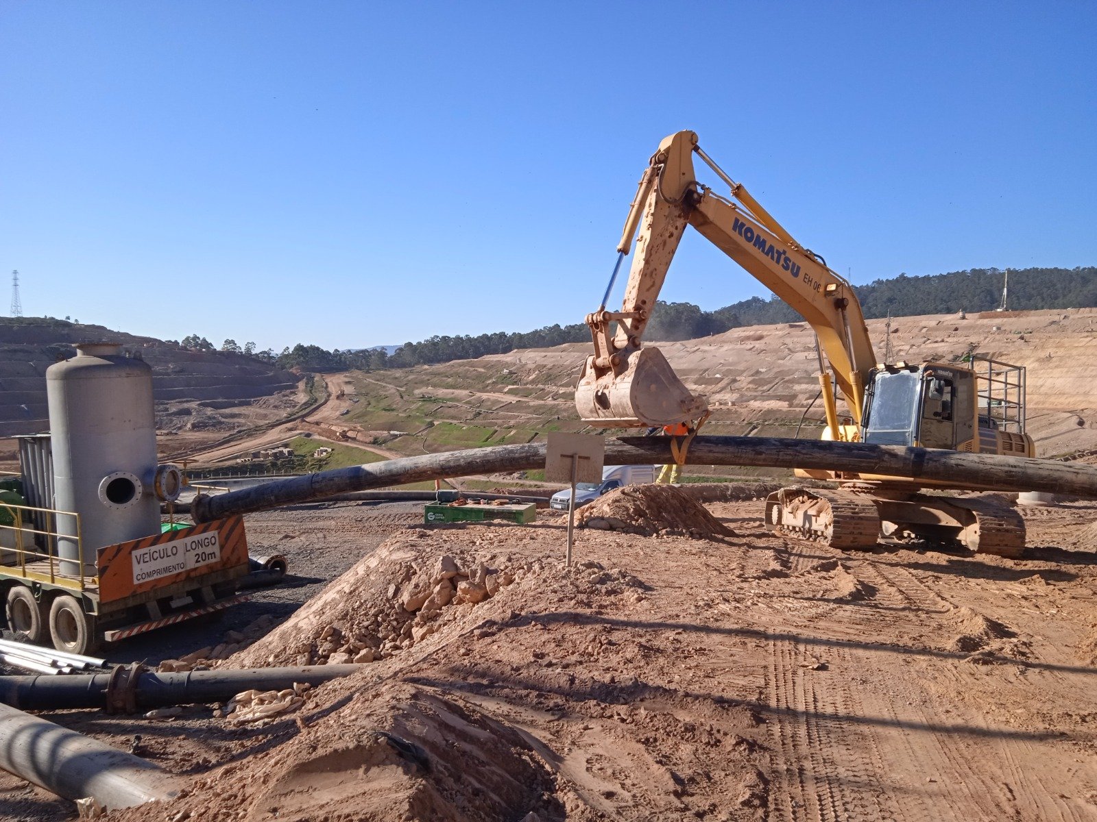 Escavadeira movimentando tubulação de grande diâmetro em aterro